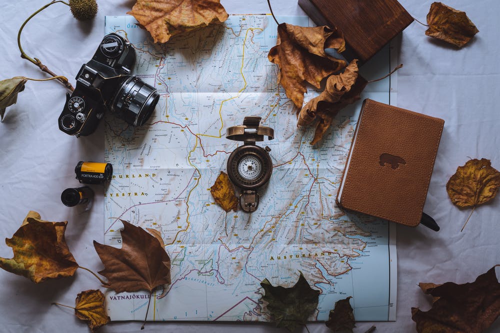 Map with camera, compass, book and fall leaves
