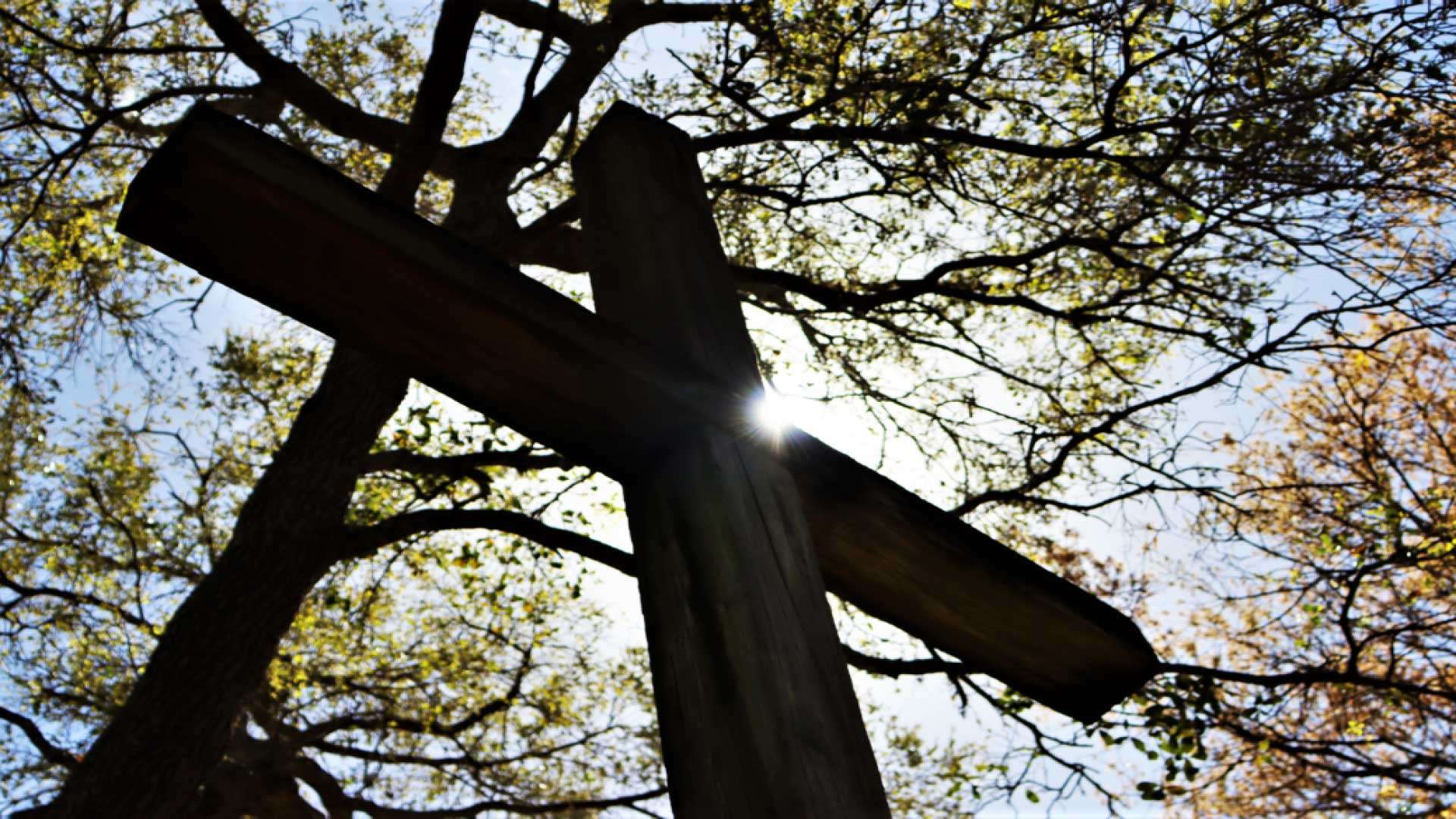 Cross in the garden silhouetted against the sky with a brilliant sun